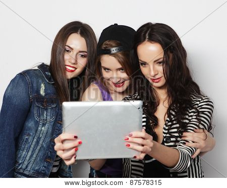Three girls friends taking selfie with digital tablet, studio shot over gray vackground
