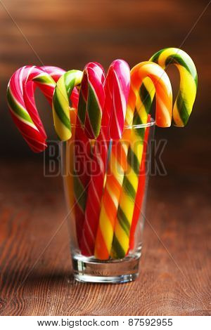Colorful candy canes in glass on table on wooden background
