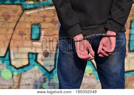Rear View Of The Arrested And Handcuffed Offender Against The Graffiti Background
