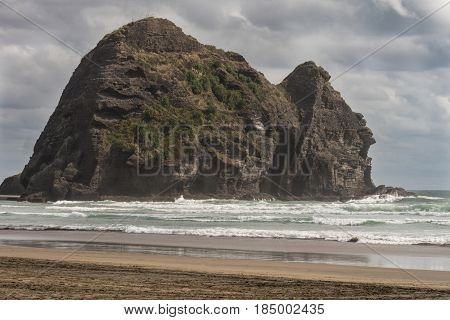 Auckland New Zealand - March 2 2017: Closeup of Rabbit rock at Piha Beach under cloudy sky and surrounded by Tasman Sea surf. Rock sea sky is all.