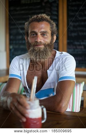 Attractive bearded curly man with a mug of smoothie is sitting in a cafe