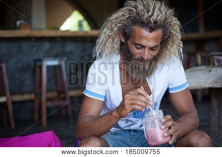 Attractive bearded curly man with a mug of smoothie is sitting in a cafe