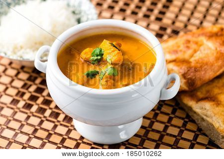 Delicious butter chicken served in a white bowl with naan bread and rice on the side on a wooden place mat.