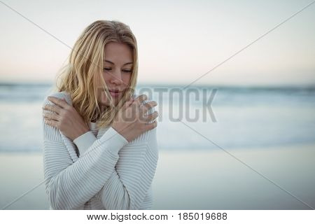 Young woman with eyes closed hugging self at beach during dusk