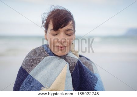 Young woman with eays closed wrapped in blanket at beach during winter