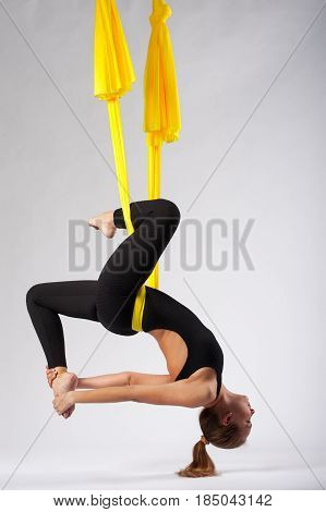 Young flexible girl working out in yellow hammock. Blonde woman practicing fly yoga or aerial acrobatics, studio shot. Body balance and antigravity training. Wellness and body care concept.