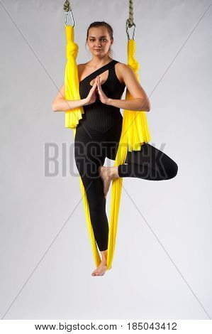 Young attractive woman performing aerial yoga. Fit girl practicing tree pose in yellow hammock. Body balance and antigravity training. Wellness and body care concept.