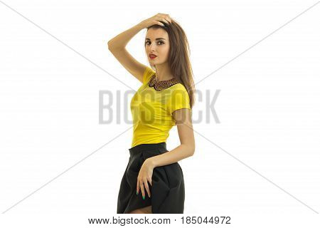 young cute girl stands sideways in a yellow t-shirt and keeping her hand on the head isolated on white background