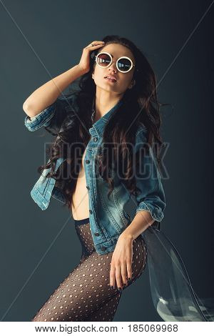 gorgeous girl in a fashionable white sunglasses, dressed in a blue jeance jacket and transparent tights without panties. posing standing near stylish transparent armchair. side view, waist portrait