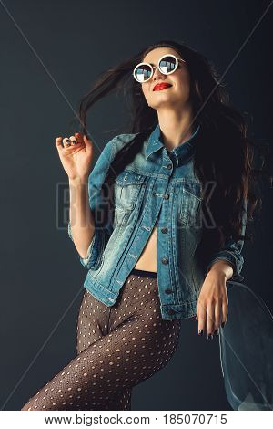 gorgeous girl in a fashionable white sunglasses, dressed in a blue jeance jacket and transparent tights without panties. posing standing near stylish transparent armchair. front view, waist portrait