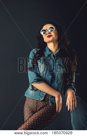 gorgeous girl in a fashionable white sunglasses, dressed in a blue jeance jacket and transparent tights without panties. posing standing near stylish transparent armchair. front view, waist portrait