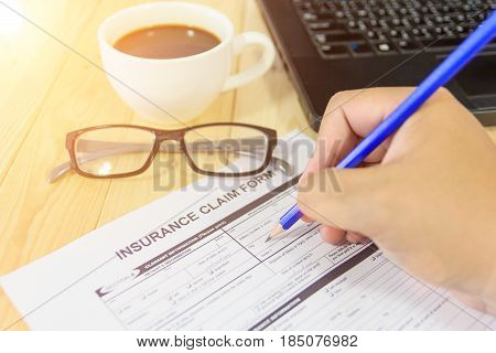 Blue pencil eyeglasses coffee cup and insurance claim form on the table. A blank form is waiting to be completed / filled and signed by a policyholder.