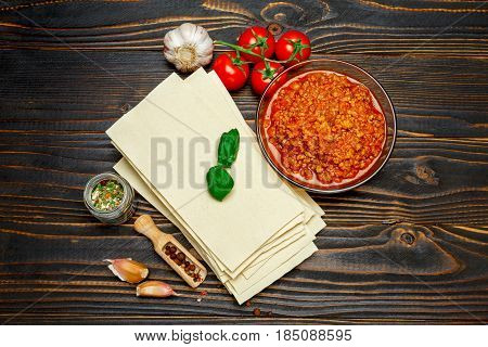 dried uncooked lasagna pasta sheets and bolognese sauce on wooden table