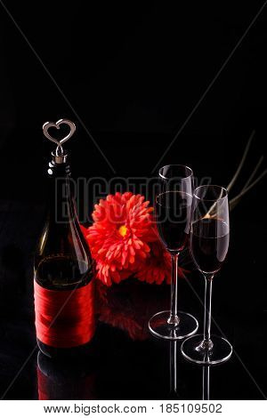 Bottle with wine, red flower, wine glasses on black background