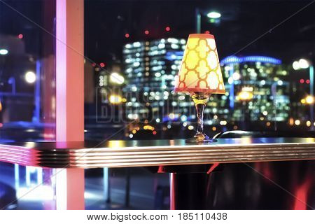 A light fixture sitting on a table at a high end club. With the nigh time Boston urban skyline in the background.