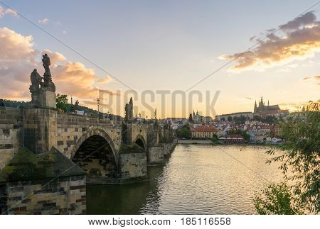 Looking across the side of the Charles Bridge in Prague at sunset with Prague Castle visible on the other side of the Vltava River.