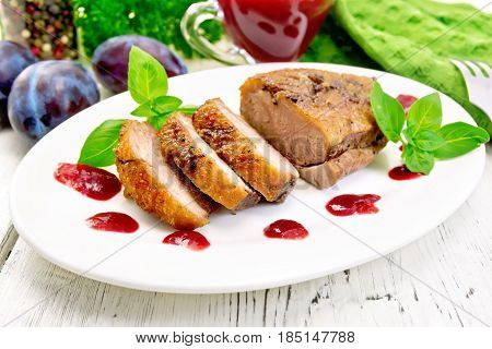 Duck breast with basil and plum sauce in a white oval plate on a wooden plank background