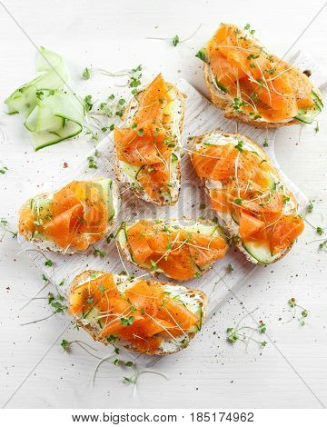 Smoked salmon bruschettas with soft cheese and cucumber shavings on white board