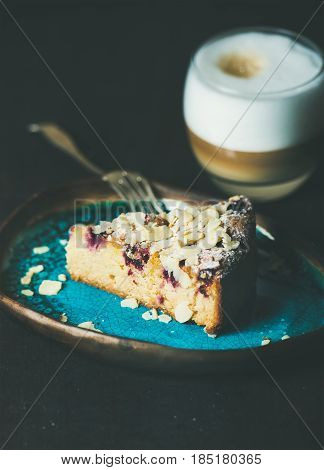 Dessert and coffee. Piece of lemon, ricotta, almond and raspberry gluten-free cake and glass of latte over dark wooden background, selective focus, vertical composition