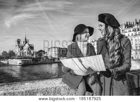 Bright in Paris. trendy mother and daughter travellers in red coats on embankment near Notre Dame de Paris in Paris France with map