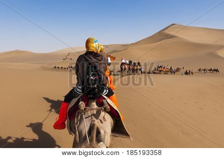 Dunhuang China - August 8 2012: Tourists on a camel caravan in the dunes around the city of Dunhuang in the ancient Silk Road in China.