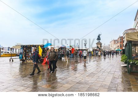 Venice Italy - April 27 2017: People are walking on a street at a port on a raining day with cloudy with The Victor Emmanuel II Monument as a background in Venice Italy.