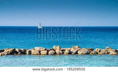 Blue sea with stones and white sailing vessel at background Cyprus