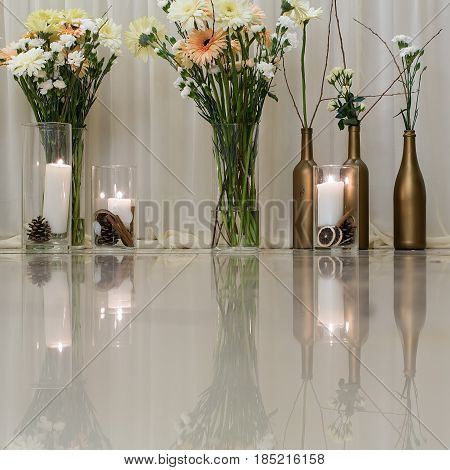 flowers. flowers bunches in glass vases and wine bottles and candles candlelight on glossy table surface indoors on white background. Celebration anniversary wedding decor
