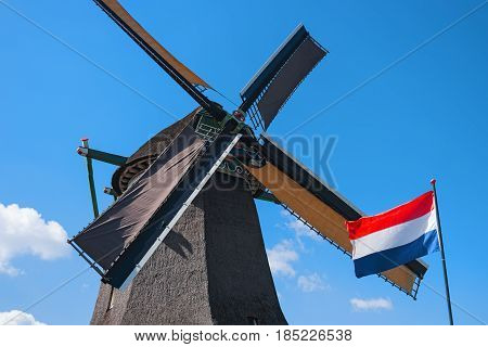 Old windmill and waving flag Zaanse Schans Netherlands. Typical dutch mill. Rural landscape. Symbol of the Netherlands