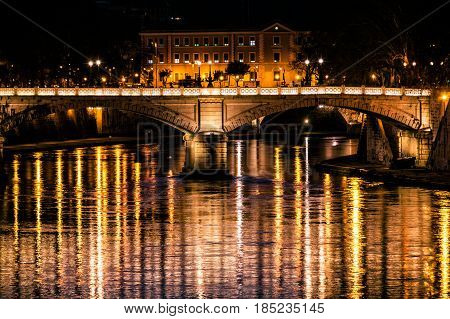 Tiber River, bridge (Ponte Giuseppe Mazzini) and reflections on water. Night. Rome, Italy. Historical building at the top.