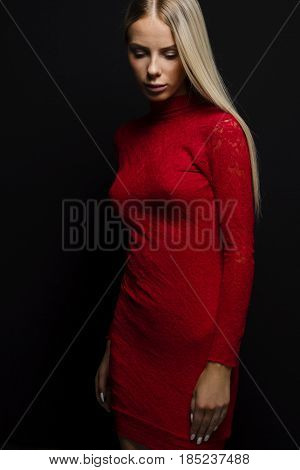 Portrait of beautiful young woman in a red dress with long blond hair standing and looking down over black background