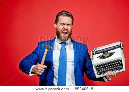 aggressive businessman hold hammer on red background business man with typewriter failure and challenge crisis and problem stress and overtime