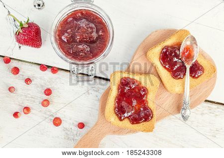 Toasts with strawberry jam for breakfast on white rusric wooden background. Top view.