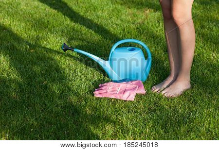 Barefoot woman standing on a freshly cut lawn , watering can and gloves 