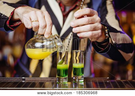 Nightclub or pub a bartender at the bar is preparing a green Mexican cocktail using a bar spoon. Hands of a bartender close-up. Horizontal photo