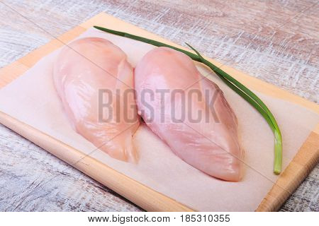 Raw chicken breast fillets and garlic ready for cooking on wooden board.