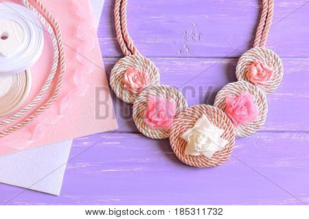 Beautiful necklace for women. Women's necklace created of ribbons, cords and felt. Materials to create accessory on a wooden table. Floral summer jewelry. Top view