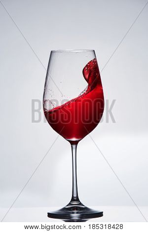Red wine splash in the delicate elegant wineglass standing against light background. Mowing wine in the pure goblet. Concept of the luxury lifestyle. Vertical photo. Viticulture, grapes and winery. Natural drink.
