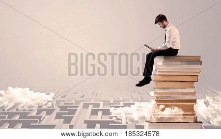 A businessman with laptop tablet in elegant suit sitting on a stack of books on top of sandy labirynth background concept