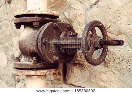 Old water valve on a background of a natural stone wall. Large and rusty valve on the water pipe close-up.