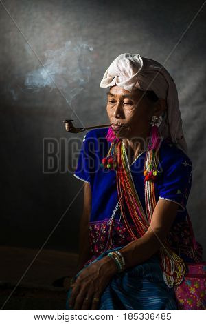 CHIANG MAI THAILAND - JUL 25 : Karen hill tribe is smoking tobacco pipe with traditional clothes and dramatic light on July 25 2015 in Chiang Mai Thailand.