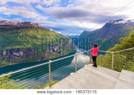 Tourism vacation and travel. Female tourist enjoying beautiful view over magical Geirangerfjorden from Flydalsjuvet viewpoint taking photo with camera Norway Scandinavia.