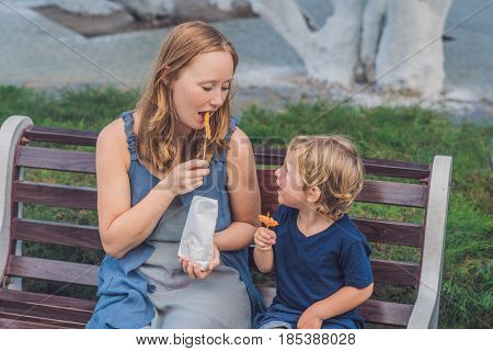 Mom And Son Eat Fried Sweet Potatoes In The Park. Junk Food Concept