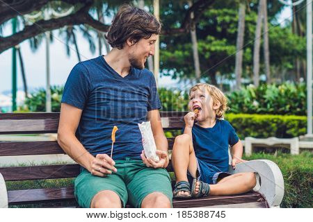 Father And Son Eat Fried Sweet Potatoes In The Park. Junk Food Concept