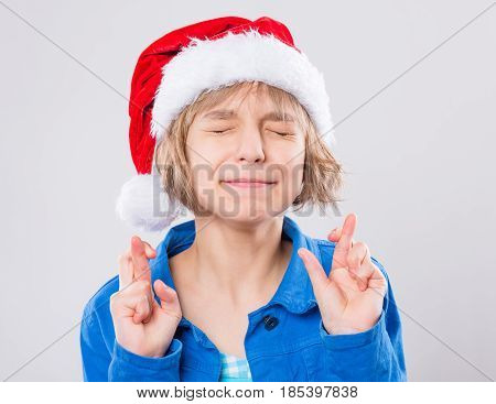 Attractive caucasian little girl wearing Santa Claus hat. Funny cute child 10 year old crossing her fingers on gray background. Child praying or making luck gesture - winter holiday christmas concept.