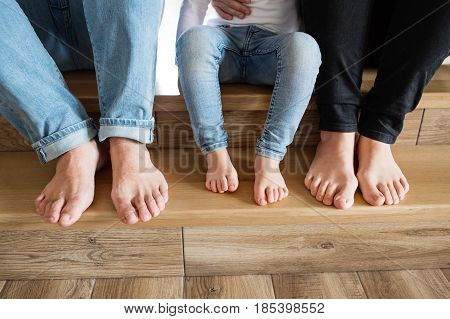 Beautiful young family sitting on stairs. Close up of bare feet of mother, father and daughter.