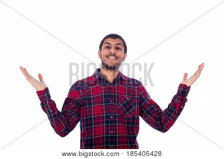 Happy friendly young man with outstretched hands feeling satisfied and wearing red caro shirt isolated on white background