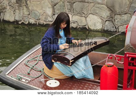 April 27 2016. Beijing China. A chinese woman sitting on a boat playing a traditional chinese instrument guzheng also known as the Chinese zithe on the water canals near houhai bar street in Beijing China.