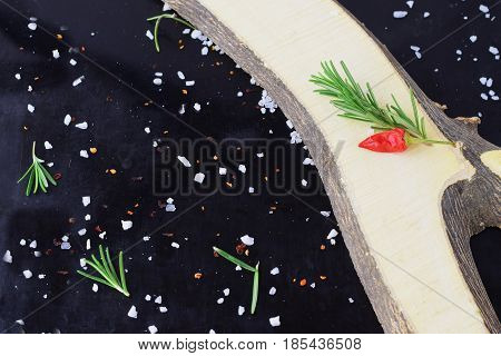 Spices and herbs on a black background with wooden element aside