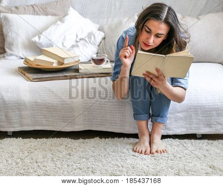 girl reading a book in a cozy room on the couch with a Cup of tea , the concept of leisure, and comfort